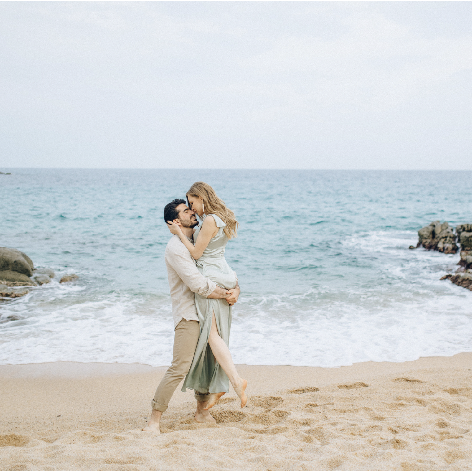 Romantic couple embracing on the rocky shore of Costa Brava with turquoise waters in the background