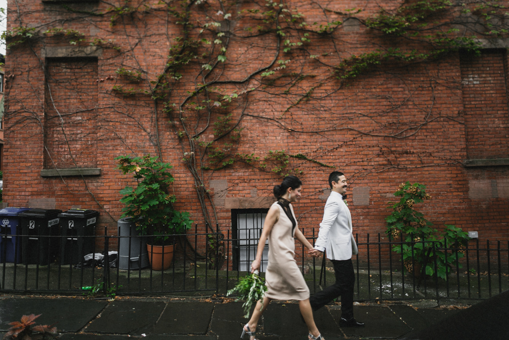 Happy bride and groom walking in front of a brick wall in Brooklyn NY