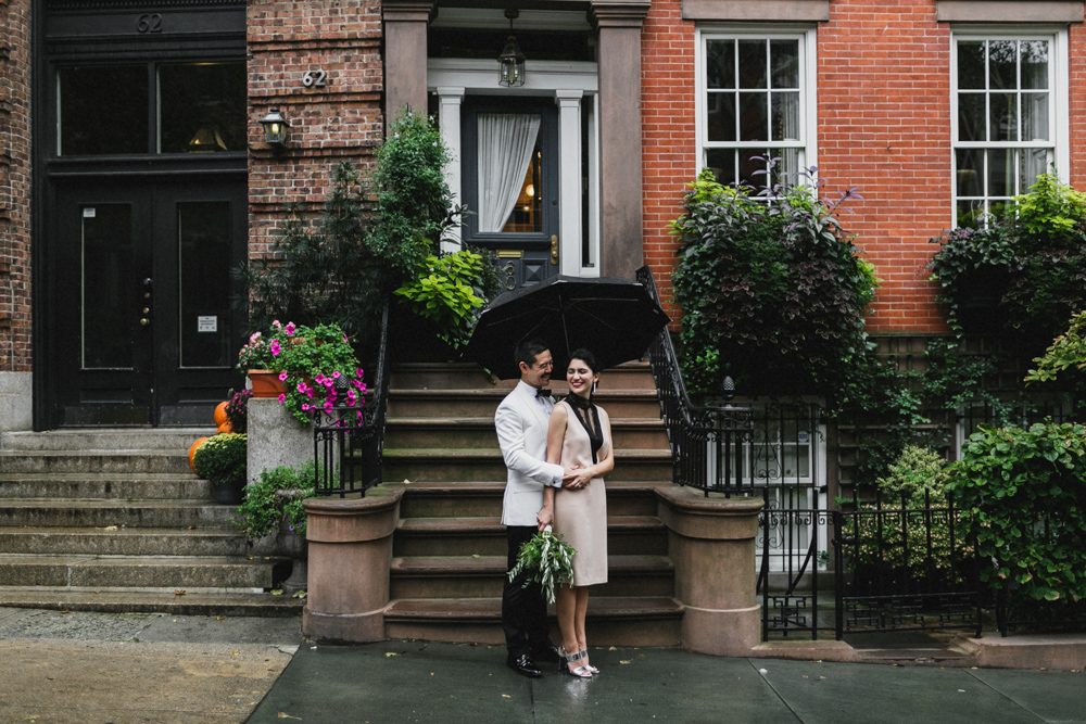 Bride and groom standing under an umbrella in front of a brownstone in Brooklyn NY