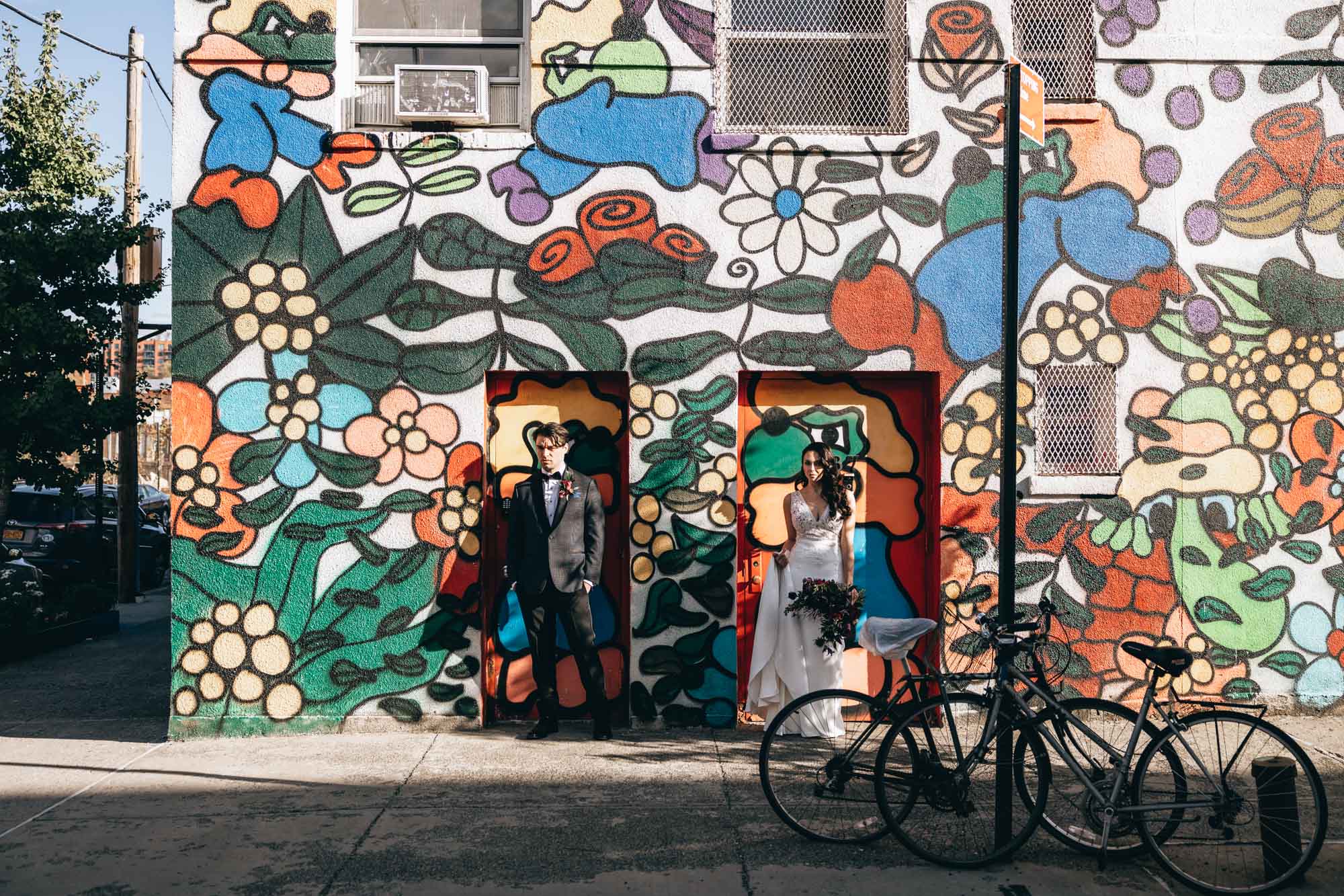 Bride and groom standing in front of a colorful floral wall full of street art. Brooklyn NY
