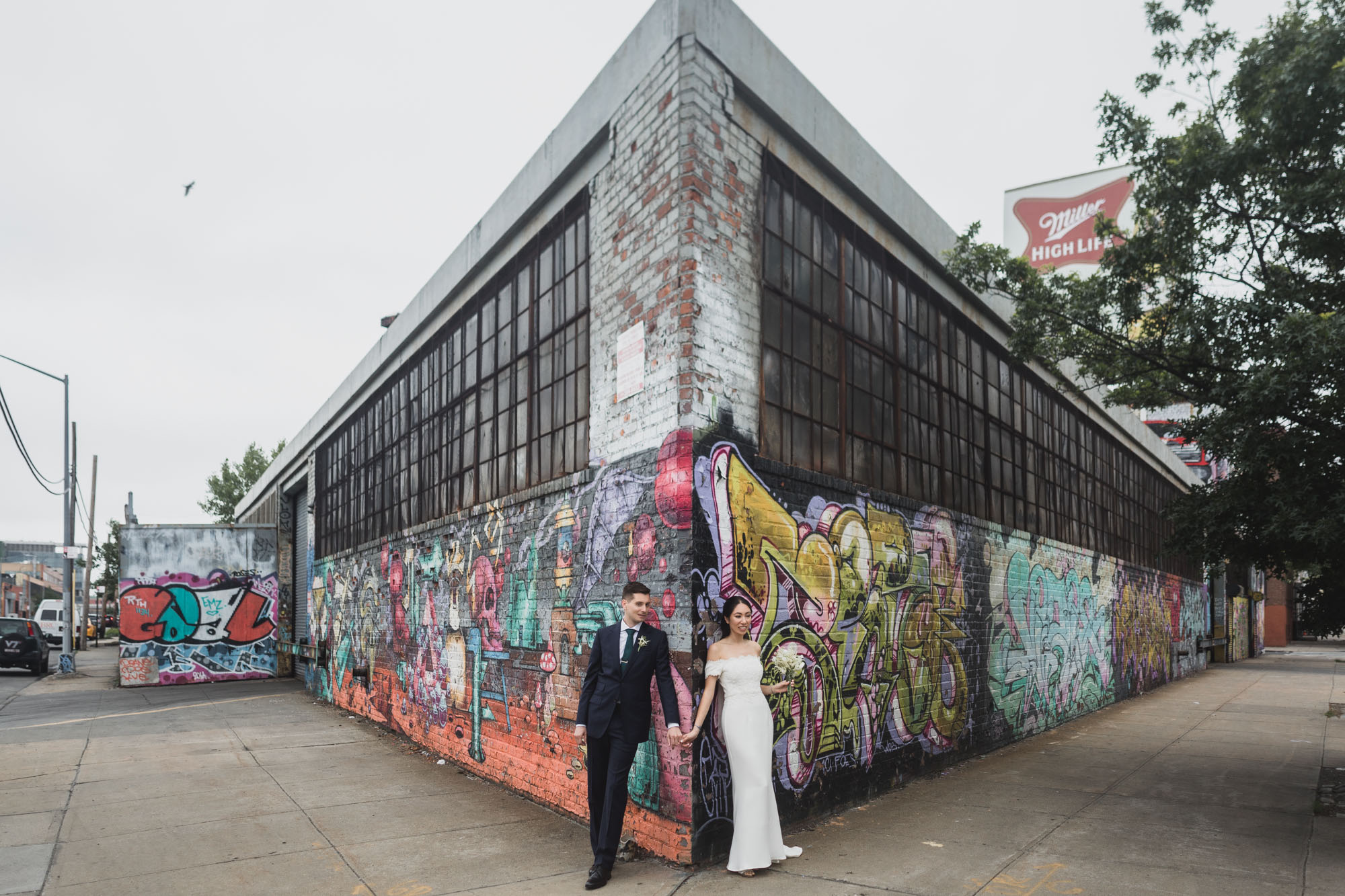 Bride and groom strolling the streets of brooklyn, amazing mural on the background.  Wedding in Williamsburg, Brooklyn