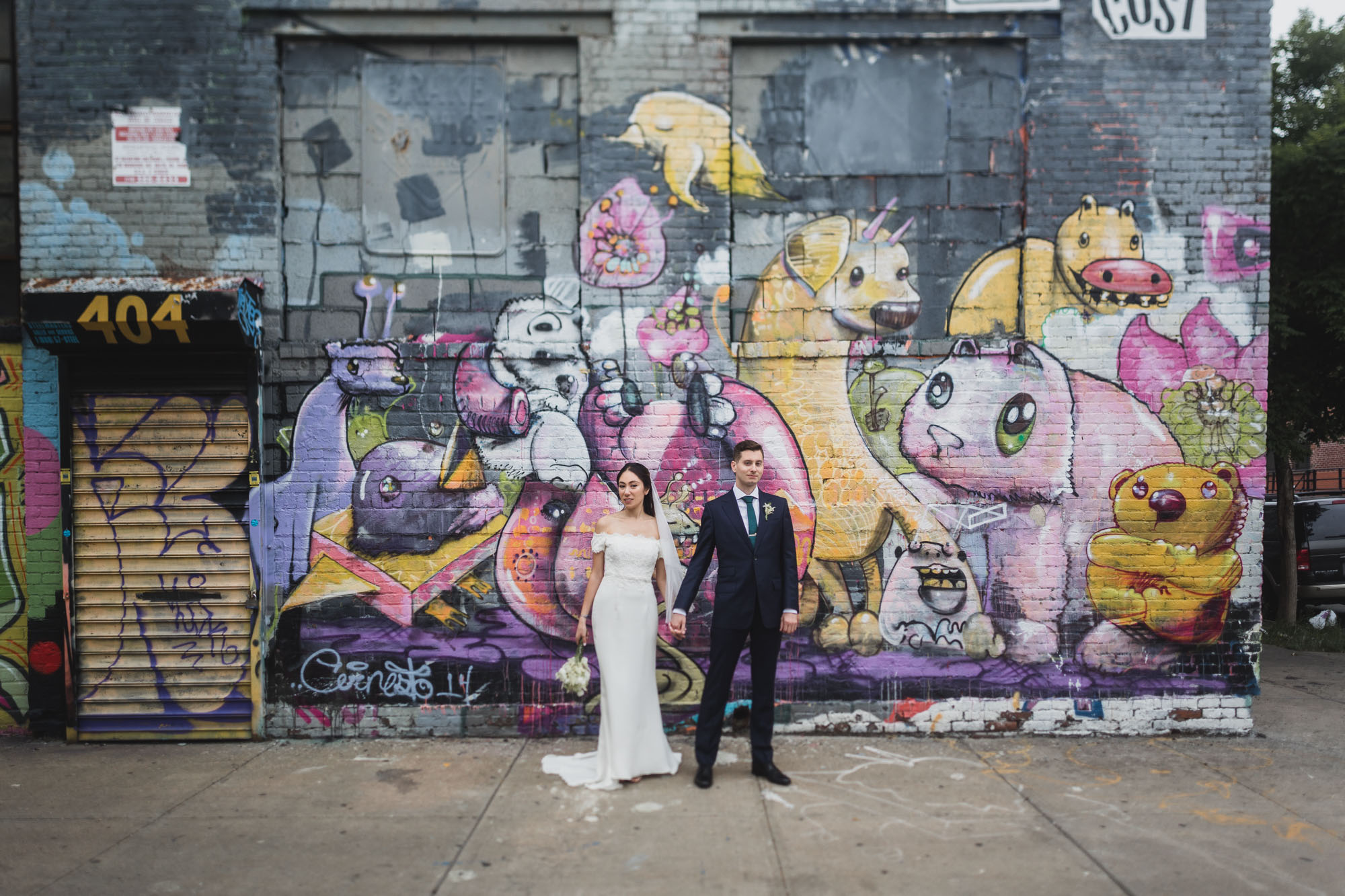 Bride and groom strolling the streets of brooklyn, amazing mural on the background.  Wedding in Williamsburg, Brooklyn