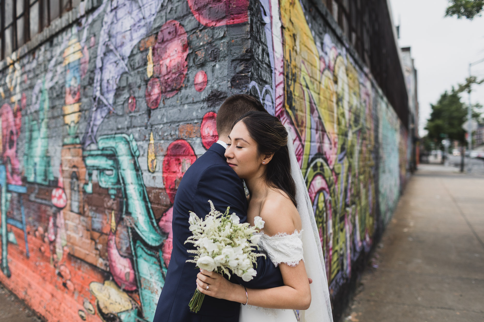 Bride and groom strolling the streets of brooklyn, amazing mural on the background.  Wedding in Williamsburg, Brooklyn