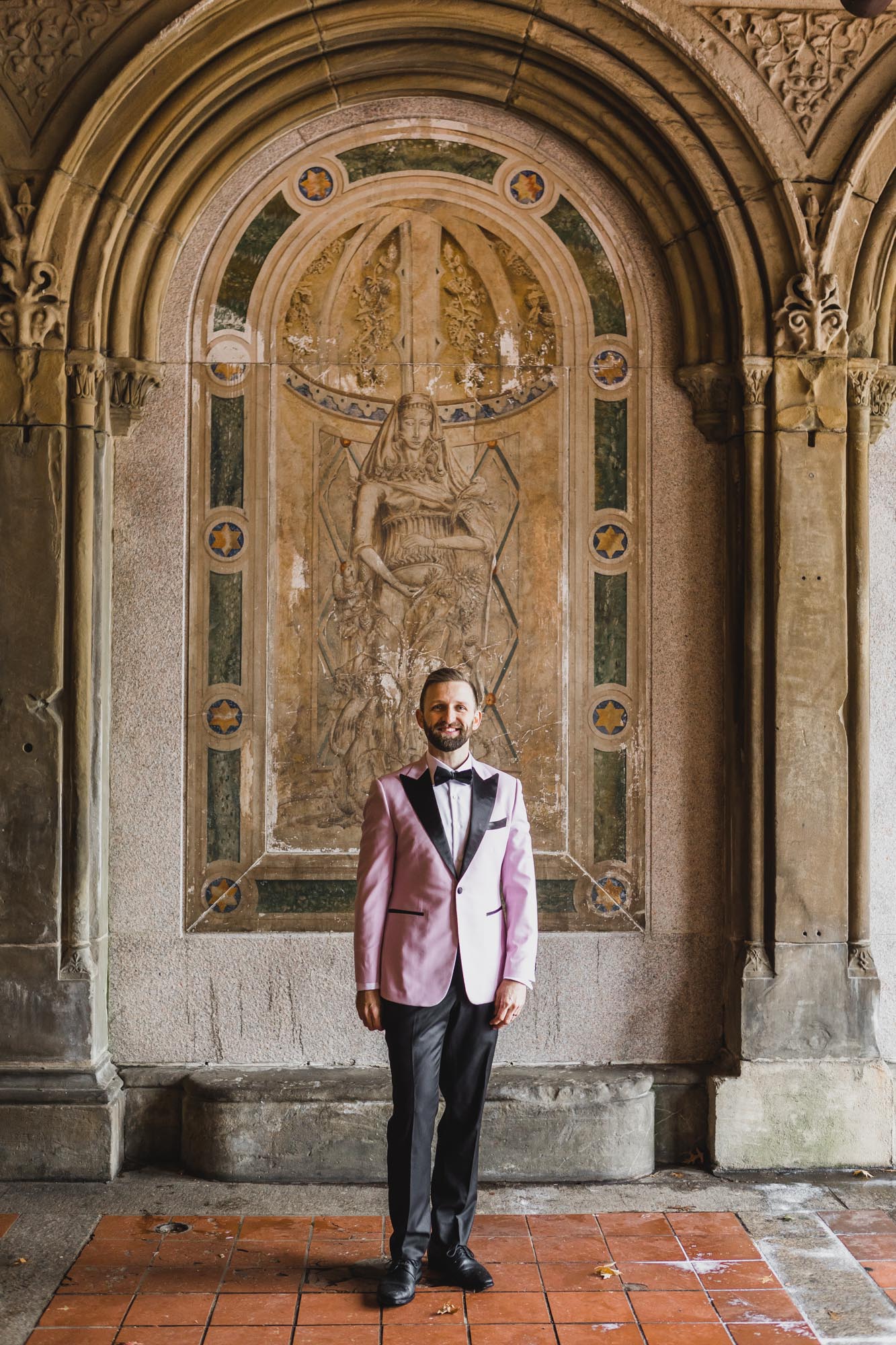 Aussie groom in a light pink suit on his wedding day at Bethesda Fountain and Terrace, Central Park. Manhattan, NY