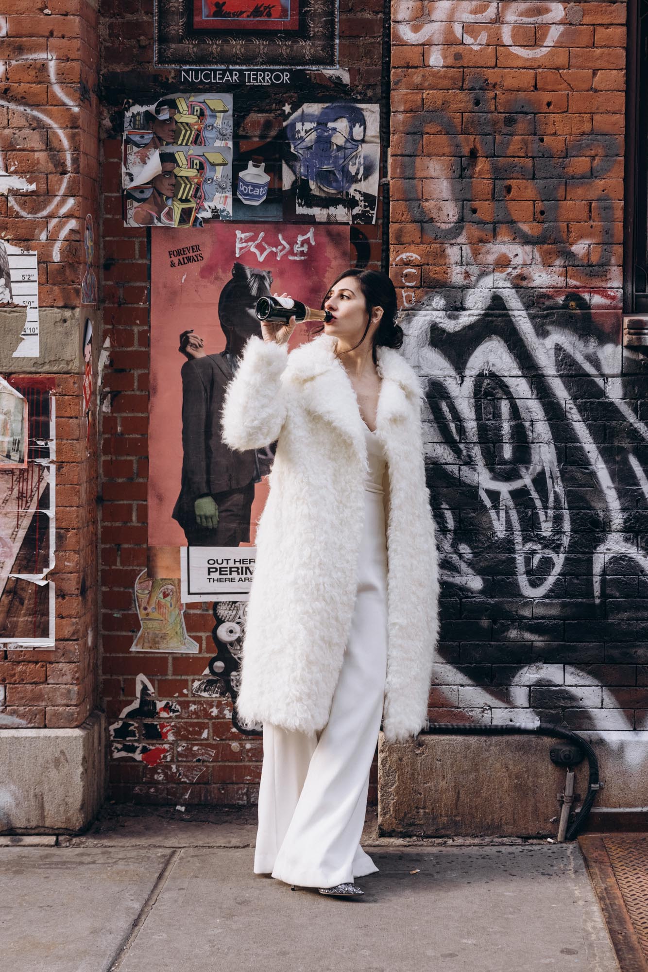 Stylish bride in a fuzzy coat with street art in the background having a drink. Soho Manhattan NY