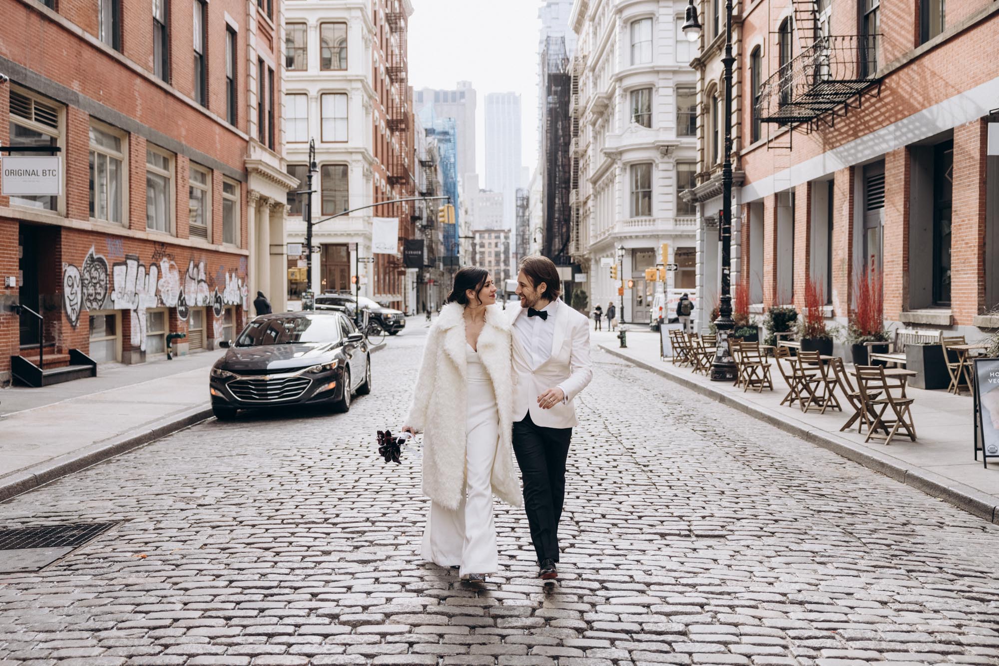Stylish bride and groom walking on a cobble stone street during their winter elopement wedding day. Soho. Manhattan, NY