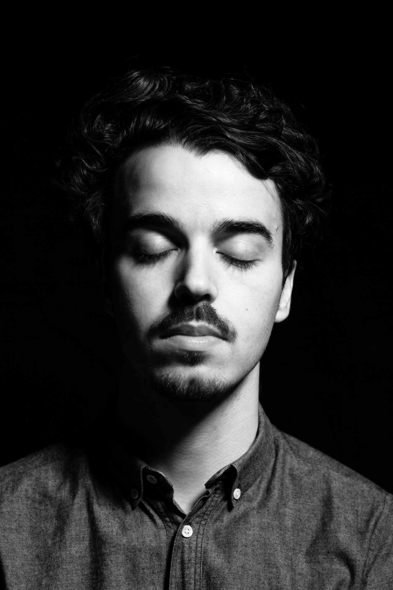 Portrait Photography Paris - Black and white headshot of a young man curly hair eyes closed on a black background